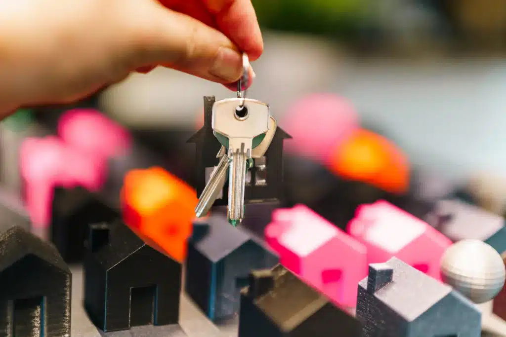 Hand hält Hausschlüssel über Miniaturhäusern – Symbolbild für Immobilienangebote